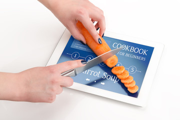 Women's hands is cutting the carrot on a tablet computer.