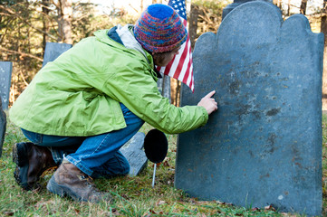 Woman reading old gravestone with flag