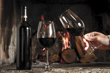 Copa de vino tinto y botella, con fuego de hogar de fondo.