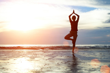 Silhouette woman practicing yoga on the beach.
