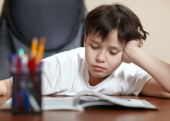 School boy studies hard over his book at home.