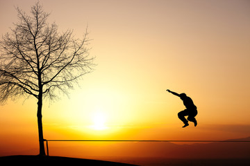 silhouette of a person jumping in the sunset on a slackline  - 51135390
