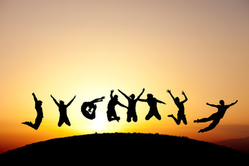 silhouetted group of friends jumping for fun in sunset
