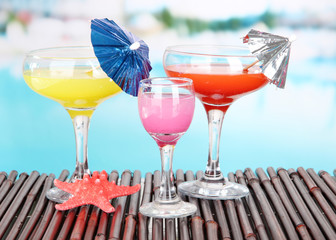 Glasses of cocktails on table near pool