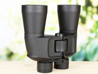 Black modern binoculars on wooden table on green background