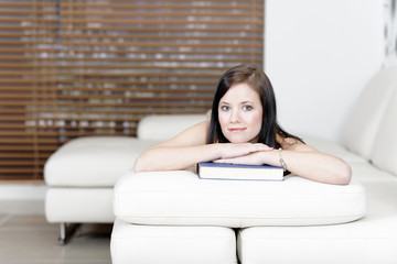 Woman lying on sofa with a book