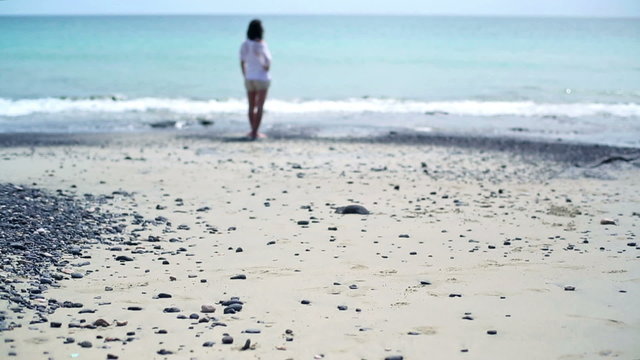 Young woman standing on the beach and looking on the sea, tilt u
