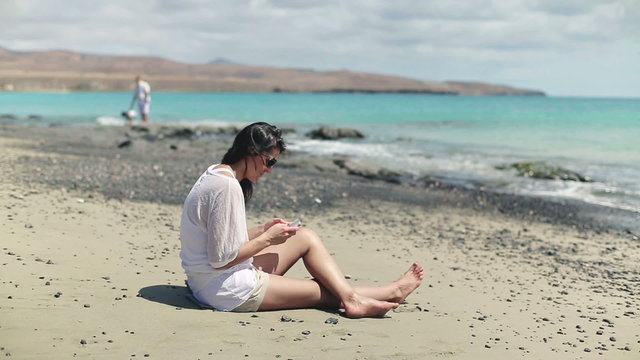 Woman sitting on the beach with cellphone, family in background