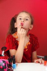 little girl in her mother's dress, is trying painting her lips