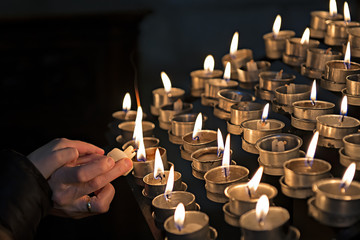 Encendiendo velas en una iglesia a modo de ofrenda. - obrazy, fototapety, plakaty
