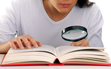 Mujer leyendo un libro sujetando una lupa.