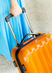 Woman in blue dress holds orange suitcase in hand