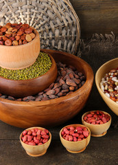 Different kinds of beans in bowls on wooden background