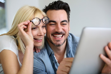 Cheerful couple websurfing on internet with tablet - obrazy, fototapety, plakaty