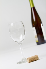 a wine glass, cork and blurred wine bottle on white