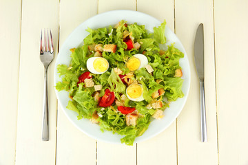 Caesar salad on white plate, on color wooden background