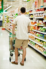 Man in a supermarket running trough the aisle with a shopping ca