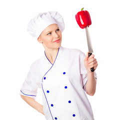 Smiling young chef in cap looking at red pepper, isolated