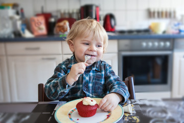 Little boy eating red cupcake