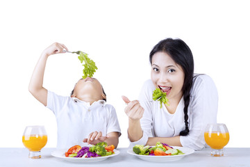 Eating vegetables with mother on white