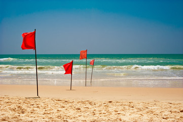 Swimming is dangerous in ocean waves. Red warning flag flapping