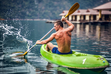 Strong young man in kayak on the picturesque lake in Thailand.