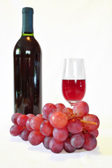 kieliszek i butelka czerwonego wina oraz winogrona