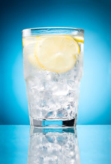 Water glass with lemon and ice isolated on a blue background