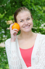 Portrait of pretty woman holding orange at summer green park.