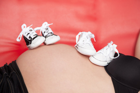 Pregnant belly with two pairs of shoes