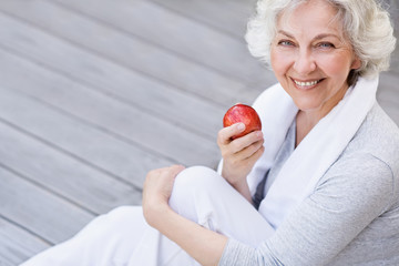 sportliche, grauhaarige Frau mit rotem Apfel