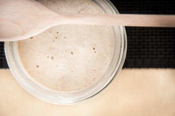 Sourdough in a glass jar on dark table mat and spoon - 51332794
