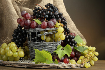 assortment of ripe sweet grapes in basket, on brown background