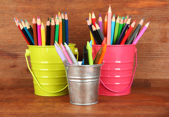 Colorful pencils in three pails on wooden background