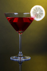 Red cocktail in martini glass on dark yellow background