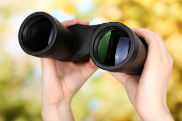 Black modern binoculars in hands on green background