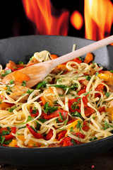 Noodles with vegetables on wok on fire background