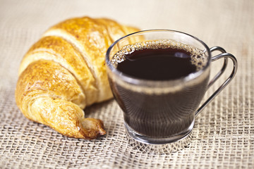 A cup of coffee with a croissant