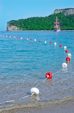 Red and white buoys and a ship with red sails. Kemer, Antalya
