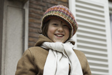 Funny young boy with long hair and hat outdoor in front of build