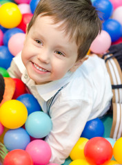 Happy little boy sitting in colourful balls