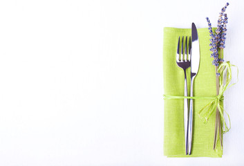 Knife and fork with green linen napkin on white wooden backgroun