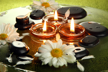 spa stones with flowers and candles in water on plate