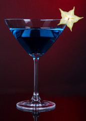 Blue cocktail in martini glass on dark red background