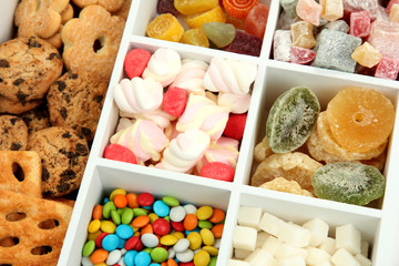 Multicolor candies and cookies in white wooden box close up