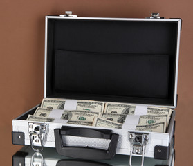 Suitcase with 100 dollar bills on brown background