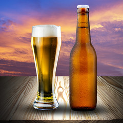 Glass and bottle of beer on wood table at sunset