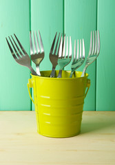 Forks in metal bucket on color wooden background