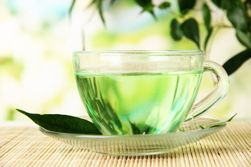 Transparent cup of green tea on bamboo mat, on nature