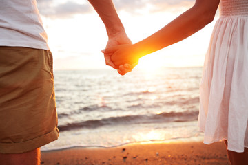 Summer couple holding hands at sunset on beach